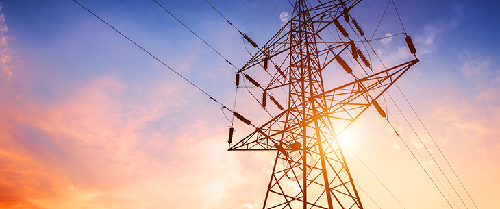 Up-angled shot of a large transmission line with the sun behind it, with pink and blue clouds